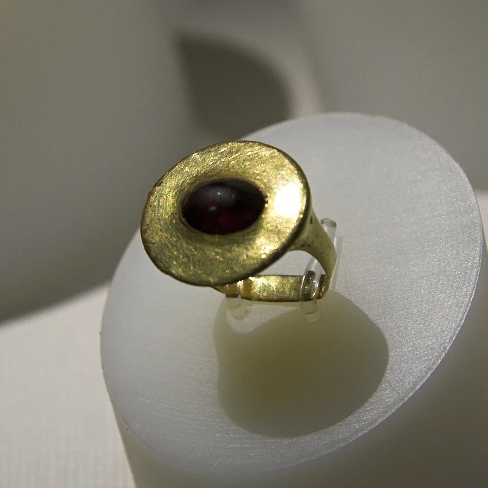 Dark-red oval stone in a broad textured yellow-metal bezel ring.