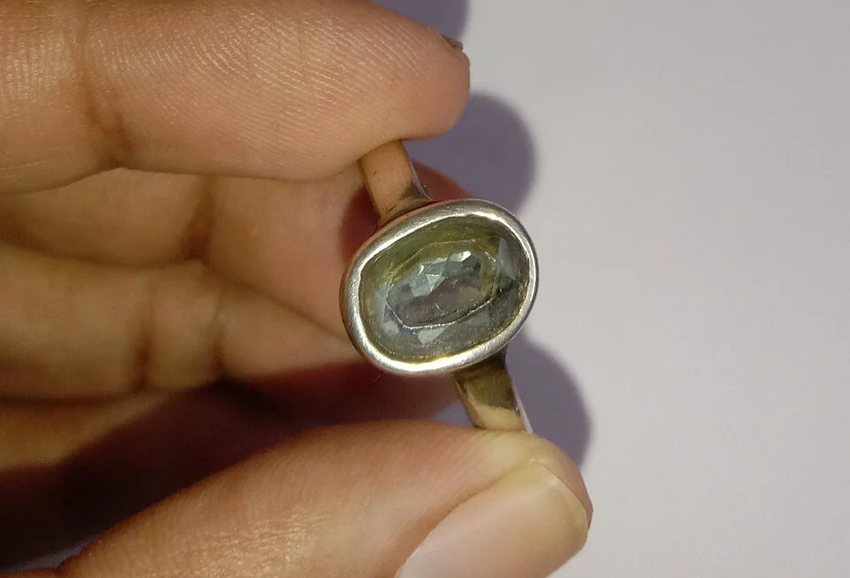 Hand holding a metal ring with a pale oval stone viewed from the side.