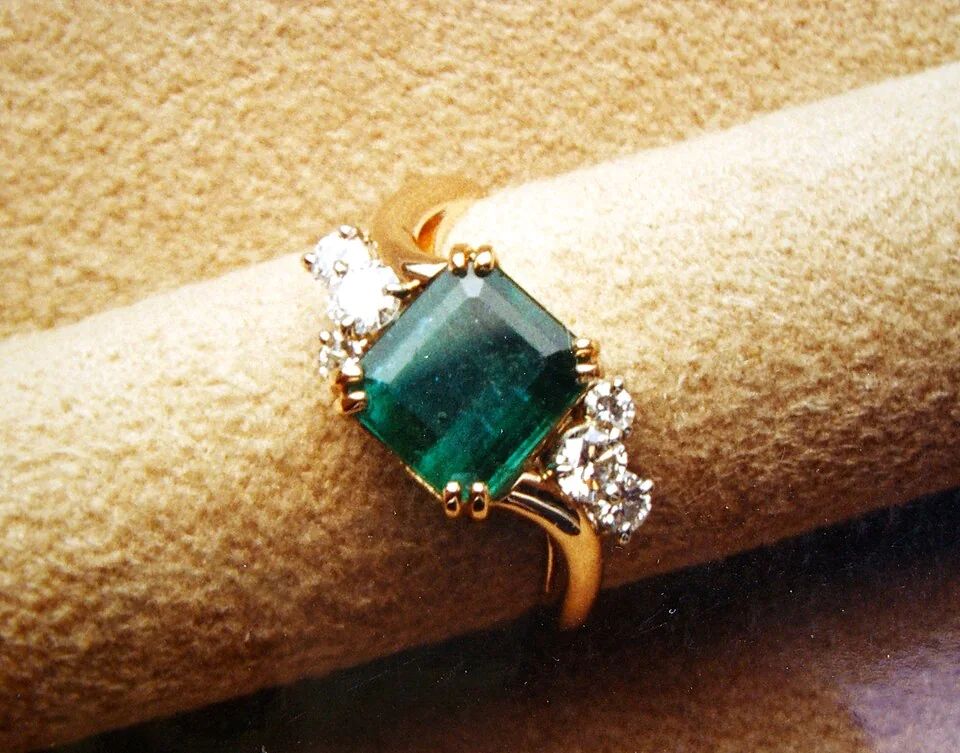 Rectangular green stone with pale side stones in a yellow-metal ring.