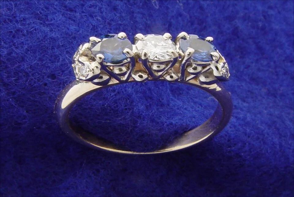 Three pale faceted stones set in a curved metal ring on blue fabric.