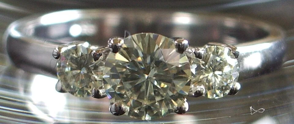 Colorless round faceted center stone with small side stones in a pale-metal ring.