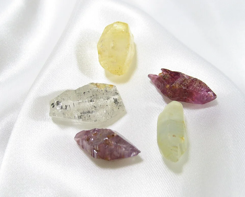 Loose pale-yellow and pink-purple rough crystals on a white surface.