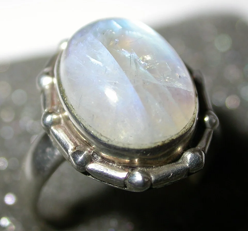 Oval pale cabochon with a bluish sheen in a sculpted metal ring setting.