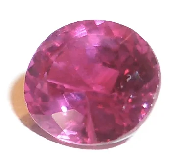 Loose pink-red round faceted stone on a white background.