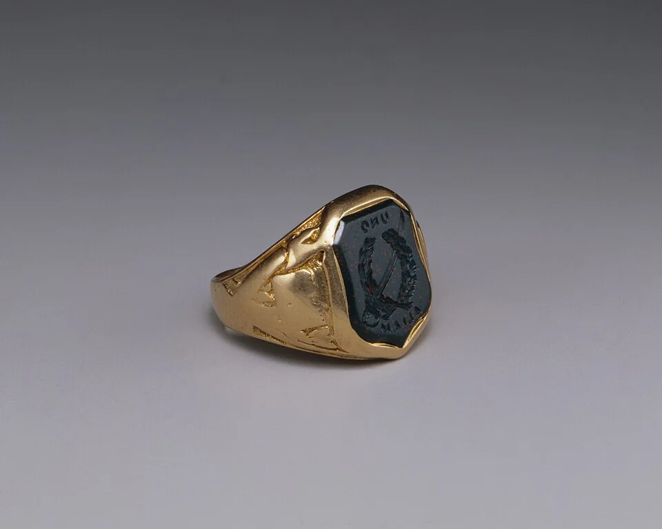 Yellow-metal signet ring with a dark engraved face, viewed at an angle.